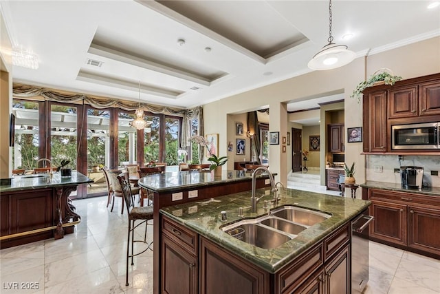 kitchen with pendant lighting, sink, appliances with stainless steel finishes, a kitchen island with sink, and a tray ceiling