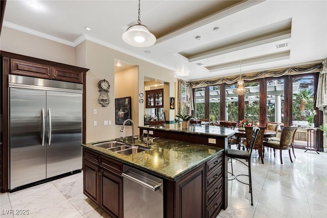 kitchen with pendant lighting, sink, appliances with stainless steel finishes, dark stone countertops, and a center island with sink