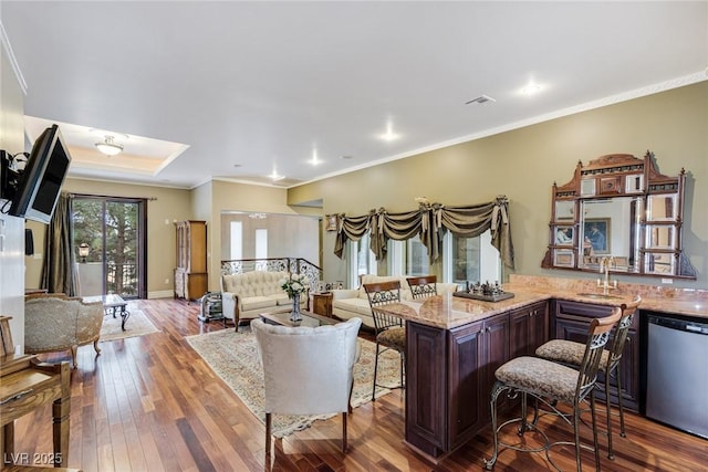 living room with a raised ceiling, ornamental molding, indoor wet bar, and light hardwood / wood-style floors