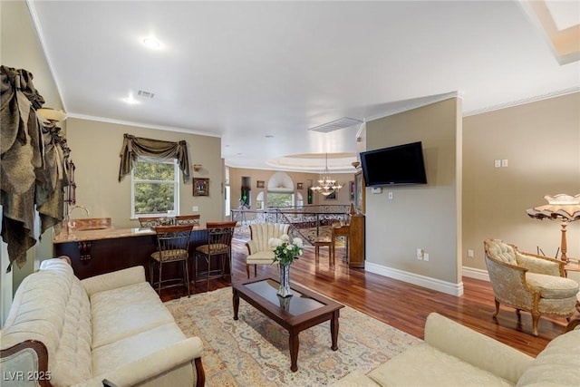 living room with an inviting chandelier, ornamental molding, sink, and hardwood / wood-style floors