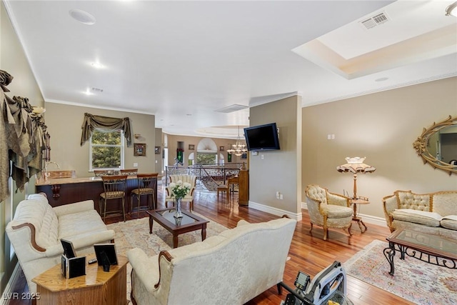 living room featuring ornamental molding, wood-type flooring, and a notable chandelier