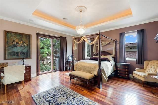 bedroom with multiple windows, access to exterior, a tray ceiling, and hardwood / wood-style flooring