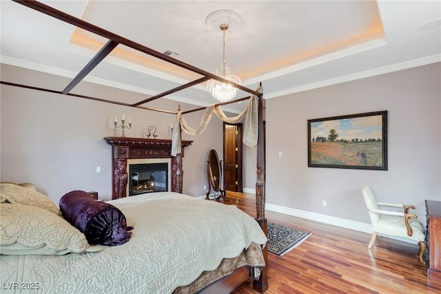 bedroom with hardwood / wood-style floors, a tray ceiling, ornamental molding, and a chandelier