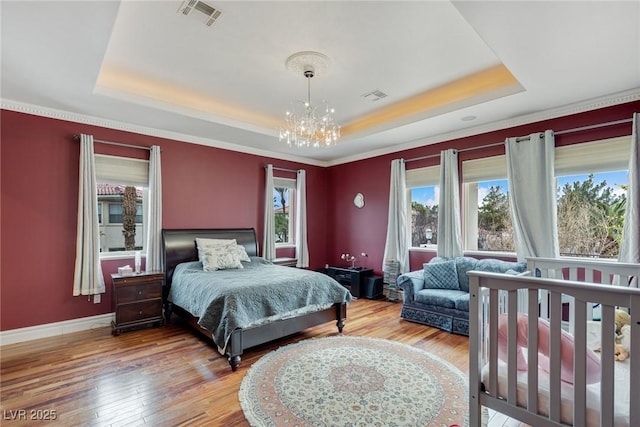 bedroom with a raised ceiling, wood-type flooring, and a notable chandelier