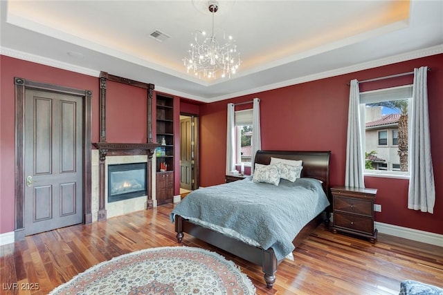 bedroom with a notable chandelier, wood-type flooring, and a raised ceiling