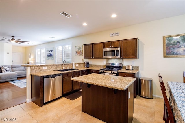 kitchen featuring dark brown cabinetry, a breakfast bar, sink, a center island, and appliances with stainless steel finishes