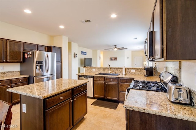 kitchen with sink, appliances with stainless steel finishes, dark brown cabinets, light stone counters, and a kitchen island