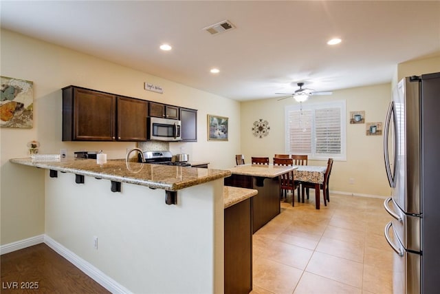 kitchen with appliances with stainless steel finishes, light stone counters, a kitchen bar, and kitchen peninsula