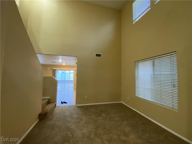 carpeted empty room featuring a towering ceiling