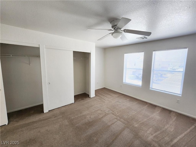 unfurnished bedroom featuring ceiling fan, carpet floors, two closets, and a textured ceiling