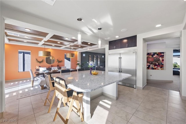 kitchen with hanging light fixtures, coffered ceiling, light stone countertops, a kitchen bar, and stainless steel built in fridge