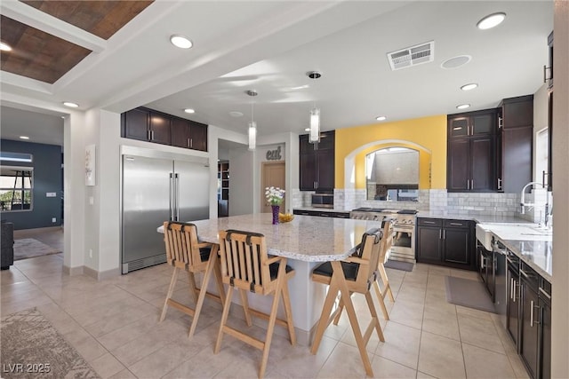 kitchen featuring pendant lighting, sink, a center island, premium appliances, and light stone countertops