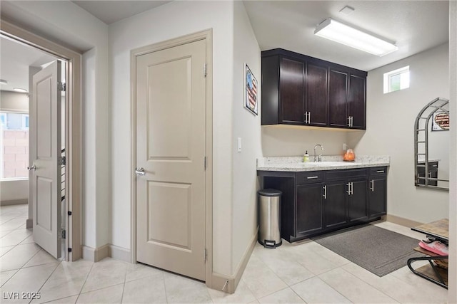 interior space with light stone countertops, sink, light tile patterned floors, and dark brown cabinets