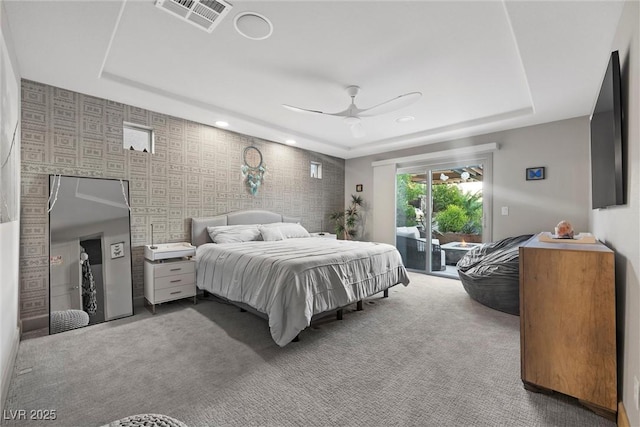 carpeted bedroom featuring access to outside, ceiling fan, and a tray ceiling