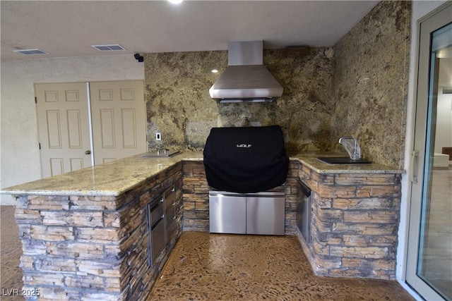 kitchen with sink, dark brown cabinets, light stone counters, kitchen peninsula, and wall chimney exhaust hood