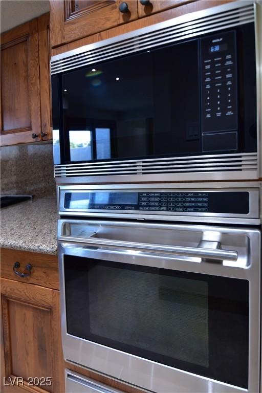 interior details with stainless steel oven, light stone countertops, and black microwave