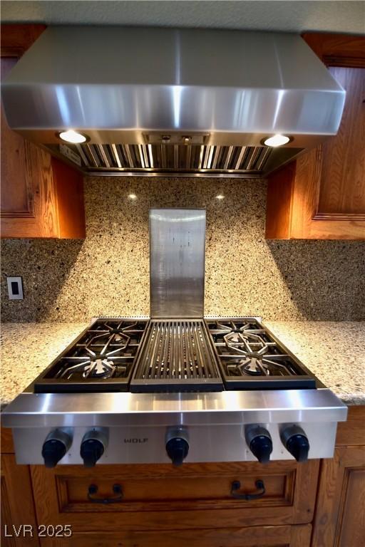 kitchen featuring light stone counters, backsplash, range hood, and stainless steel gas cooktop