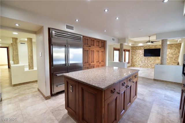 kitchen featuring light stone countertops, stainless steel built in refrigerator, a kitchen island, and ceiling fan