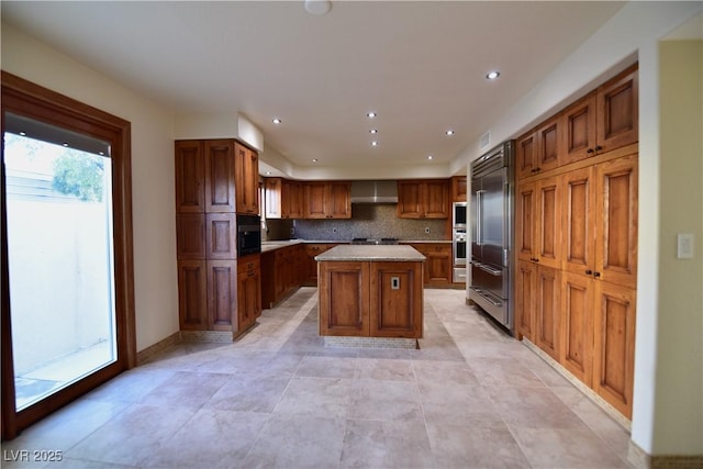 kitchen featuring wall chimney exhaust hood, built in appliances, a center island, and decorative backsplash