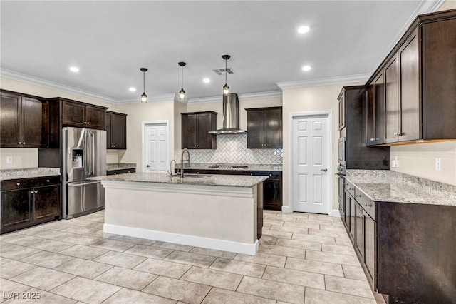 kitchen with sink, hanging light fixtures, appliances with stainless steel finishes, a kitchen island with sink, and wall chimney range hood