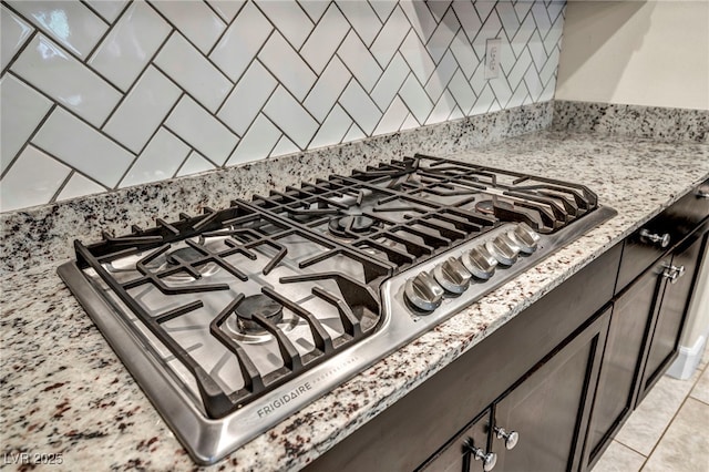 interior details with dark brown cabinetry, decorative backsplash, light stone countertops, and stainless steel gas cooktop