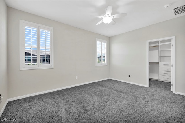 unfurnished bedroom featuring dark colored carpet, a walk in closet, ceiling fan, and a closet