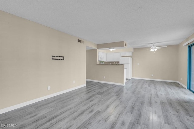 unfurnished living room with a textured ceiling, ceiling fan, and light wood-type flooring