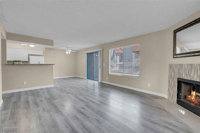 unfurnished living room with a textured ceiling, ceiling fan, and light hardwood / wood-style flooring