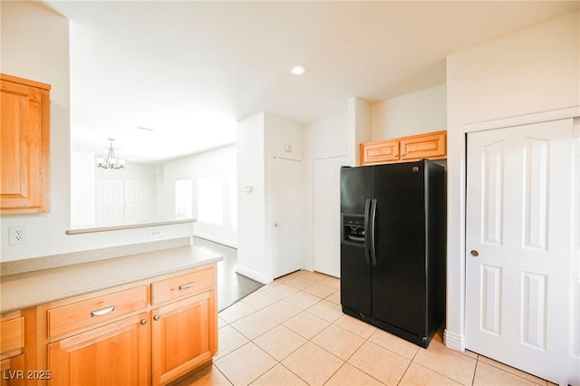 kitchen with a notable chandelier, black fridge with ice dispenser, light brown cabinets, and light tile patterned floors