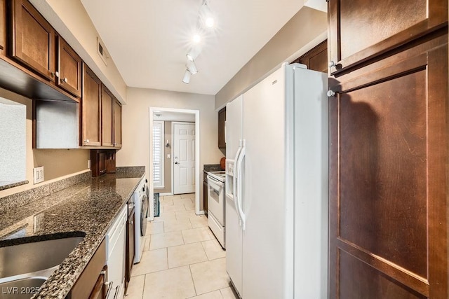 kitchen with dark stone countertops, white appliances, track lighting, and light tile patterned flooring