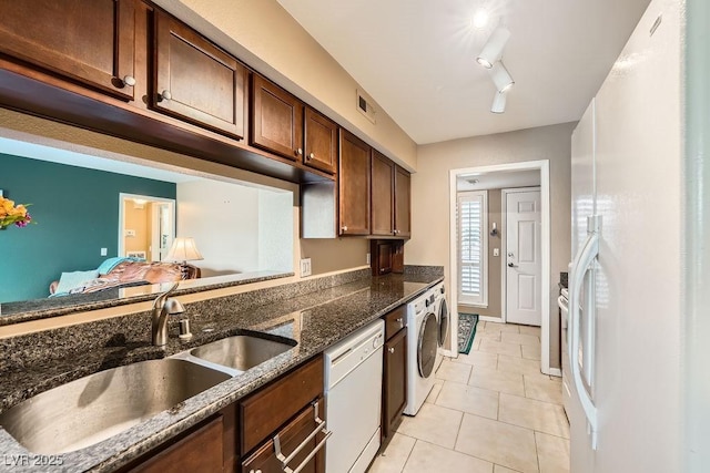 kitchen with washer / dryer, sink, dark stone countertops, light tile patterned floors, and white appliances