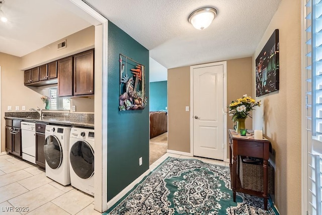 clothes washing area with light tile patterned floors, washer and clothes dryer, sink, and a textured ceiling