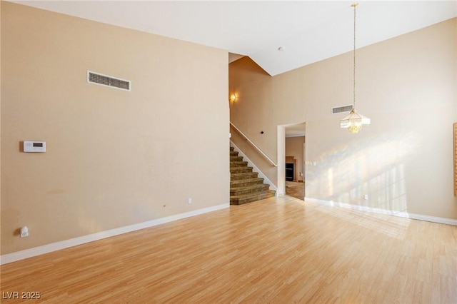 unfurnished living room with wood-type flooring, a notable chandelier, and high vaulted ceiling