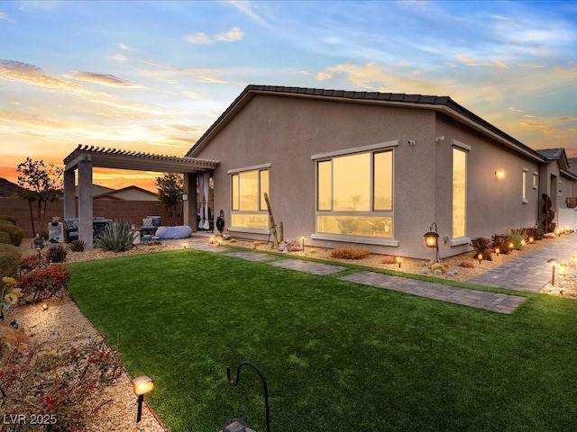 back house at dusk with a pergola and a lawn