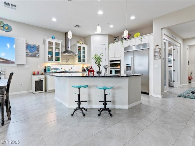 kitchen featuring wall chimney exhaust hood, white cabinetry, decorative light fixtures, a kitchen island, and stainless steel appliances