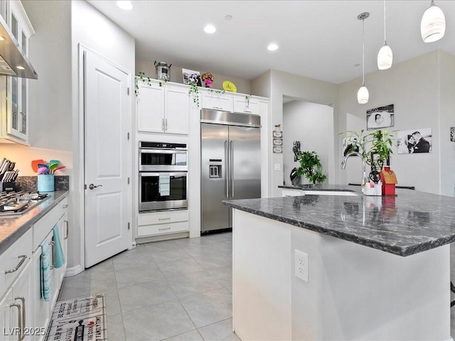 kitchen featuring wall chimney range hood, light tile patterned floors, hanging light fixtures, stainless steel appliances, and white cabinets