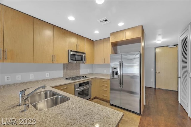 kitchen with sink, light hardwood / wood-style flooring, appliances with stainless steel finishes, light stone counters, and kitchen peninsula