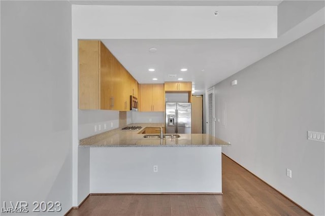 kitchen featuring stainless steel appliances, kitchen peninsula, light hardwood / wood-style flooring, and light brown cabinets