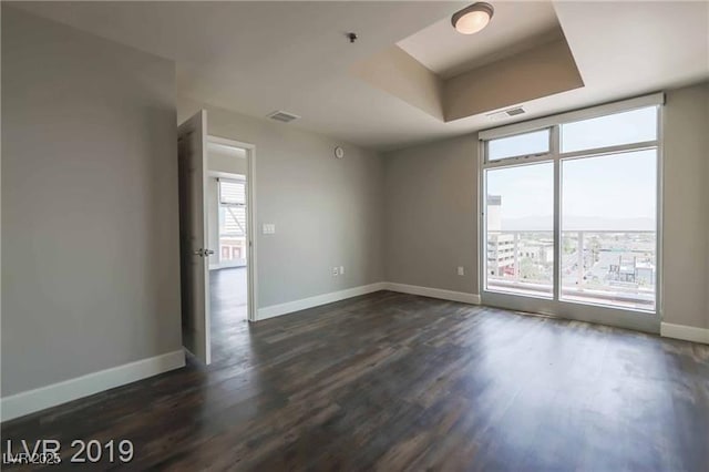 spare room with a tray ceiling and dark hardwood / wood-style floors