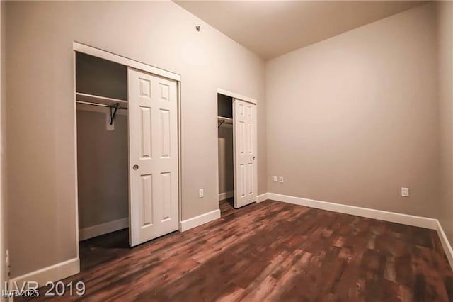 unfurnished bedroom with two closets and dark wood-type flooring