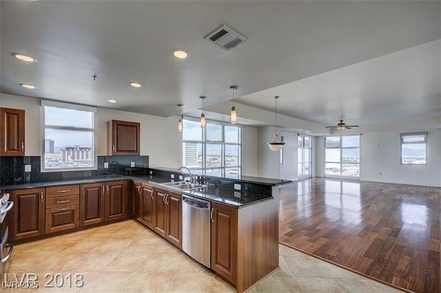 kitchen featuring decorative light fixtures, dishwasher, sink, dark stone counters, and kitchen peninsula