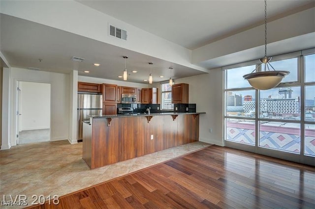 kitchen featuring pendant lighting, appliances with stainless steel finishes, a kitchen bar, kitchen peninsula, and light wood-type flooring