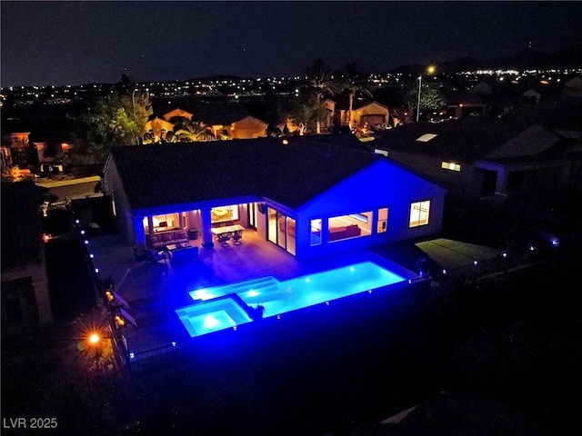 back house at twilight featuring a pool with hot tub, a fireplace, and a patio