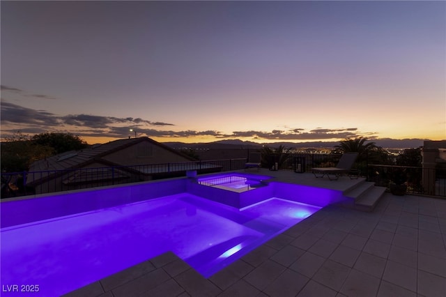 pool at dusk featuring an in ground hot tub and a patio