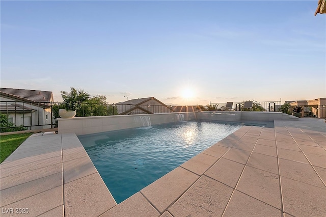 pool at dusk with pool water feature and a patio area