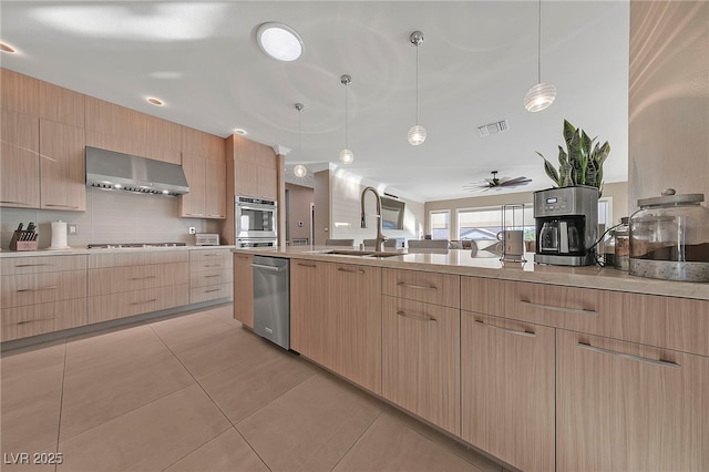 kitchen featuring sink, hanging light fixtures, light brown cabinets, stainless steel appliances, and wall chimney range hood