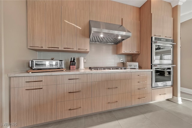 kitchen featuring backsplash, stainless steel appliances, wall chimney exhaust hood, and light brown cabinets