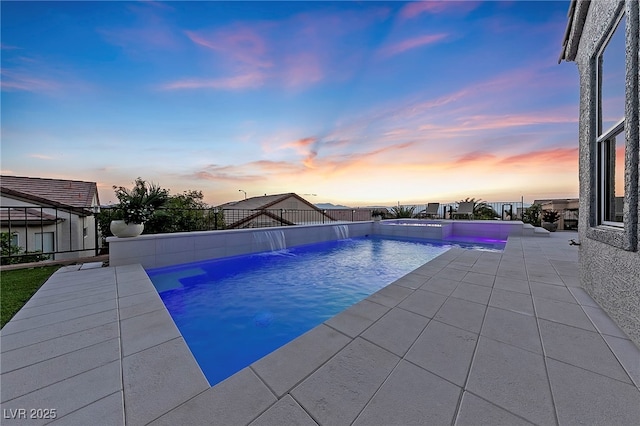 pool at dusk with pool water feature and a patio area