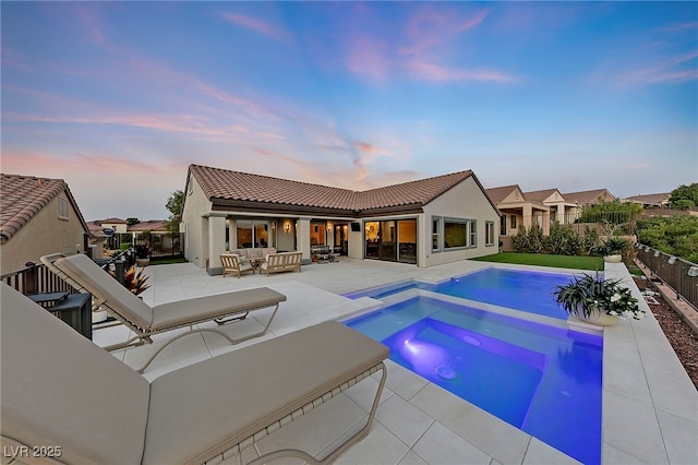 pool at dusk with an in ground hot tub, an outdoor hangout area, and a patio