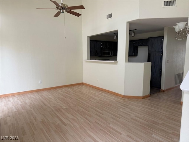 unfurnished living room featuring a towering ceiling, wood-type flooring, and ceiling fan with notable chandelier